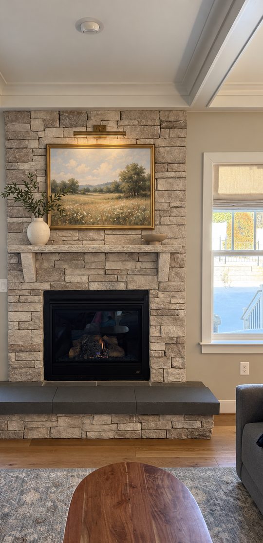 The same fireplace with the stone lightened, a framed landscape painting and a brass picture light